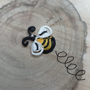 May include: A handmade bee-shaped applique with black, white, and yellow thread. The bee has a detailed design with the word "vizz" and "vizzz" written above it. A black swirl is drawn next to the bee.