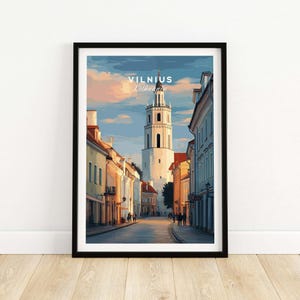 Puede incluir: Impresión artística enmarcada que representa una escena callejera en Vilna, Lituania. La obra de arte muestra una alta torre blanca y edificios que bordean una calle adoquinada bajo un cielo azul y naranja. La palabra "Vilnius" está impresa en la parte superior.