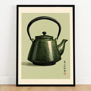 May include: A framed wall art print featuring a speckled dark green teapot with a black arched handle and lid. The teapot is centred against a light sage green background. Vertical Japanese calligraphy text and a small red seal appear in the lower right.