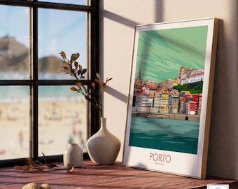 May include: A framed travel poster of Porto, Portugal, featuring a colorful illustration of the city's waterfront buildings. The poster is displayed on a wooden surface next to a window with a view of a beach. A vase with a plant is also on the surface.