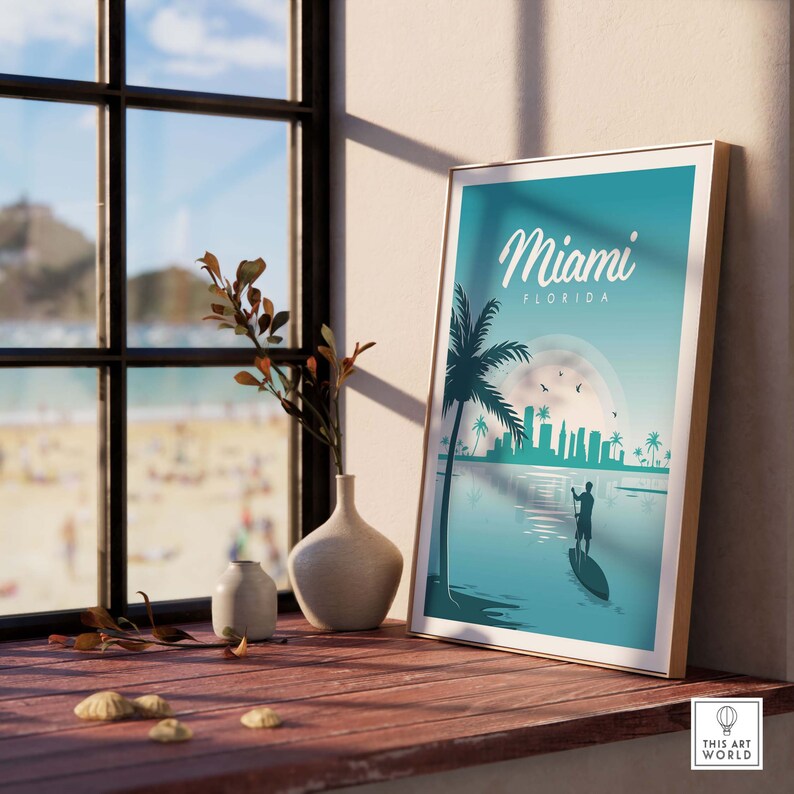 May include: A teal blue poster with a white frame featuring a silhouette of a person paddleboarding in front of a cityscape with the text "Miami, Florida" in white.