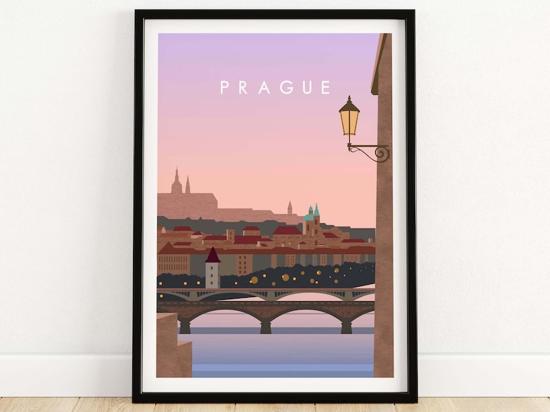 May include: Framed art print featuring a stylized illustration of Prague, Czech Republic. The artwork depicts the city skyline with bridges, buildings, and a street lamp against a pink and purple sky. The word "PRAGUE" is at the top.