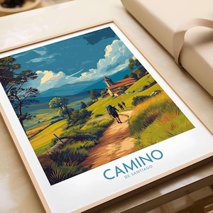 May include: A framed art print featuring a vibrant landscape illustration of a hiking trail. The artwork depicts a path winding through a green hillside, with a church and mountains in the background. The words "CAMINO DE SANTIAGO" are printed in blue.