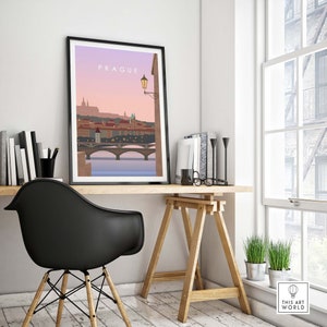May include: Framed art print of Prague, featuring a minimalist illustration of the city's skyline, bridges, and buildings. The print has a black frame and is displayed on a wooden desk with a black chair. The text "PRAGUE" is at the top.
