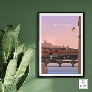 May include: A framed art print featuring a stylized illustration of Prague. The artwork depicts the city's skyline with bridges, buildings, and a warm sunset sky. The word "PRAGUE" is printed at the top. A street lamp is visible on the right.