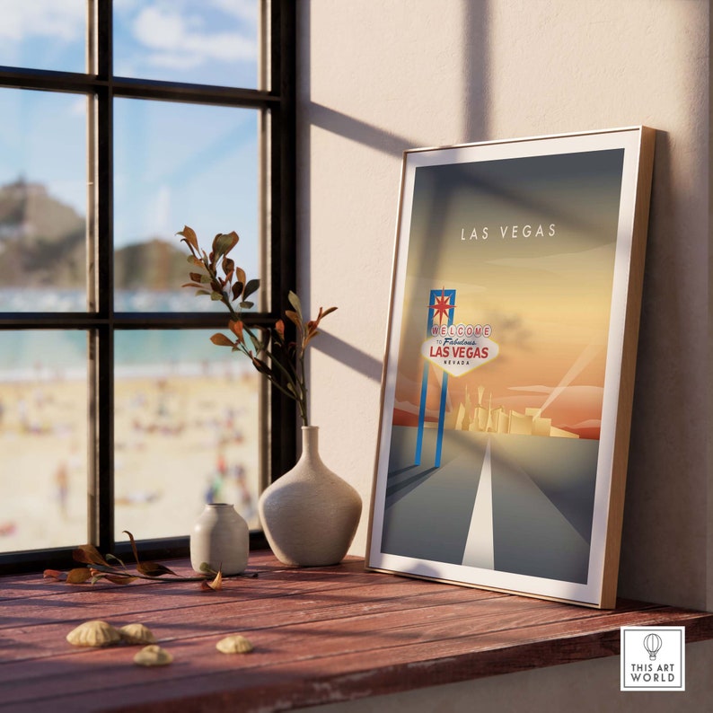 May include: A retro-style poster with a sunset background and a road leading to the iconic "Welcome to Fabulous Las Vegas" sign. The poster is framed and displayed on a wooden surface with a vase and a small vase with dried branches.