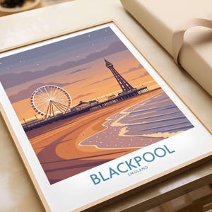 May include: A framed art print featuring a stylized illustration of Blackpool, England. The image showcases a Ferris wheel, a tower, and a pier on a beach at sunset. The word "BLACKPOOL" is printed in blue at the bottom of the print.