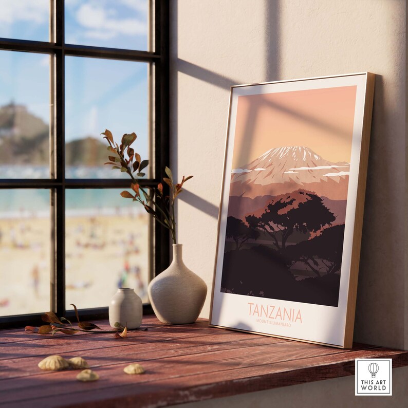 Puede incluir: Un p&oacute;ster minimalista con una cordillera de monta&ntilde;as en el fondo y un solo &aacute;rbol en primer plano. El p&oacute;ster est&aacute; enmarcado en un marco de madera clara y tiene el texto "TANZANIA" y "KILIMANJARO" en una fuente blanca sans-serif.