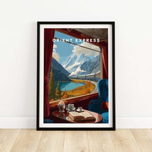May include: Framed art print depicting the interior of a train carriage with a scenic mountain view. The text "ORIENT EXPRESS" is visible. A table with a book, teacups, and a glass is in the foreground. A blue armchair is on the right.