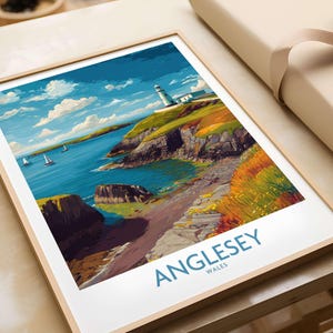 Puede incluir: Lámina artística enmarcada que presenta un paisaje costero con un faro. La obra muestra una escena vibrante con agua azul, acantilados verdes y un cielo brillante. La impresión está etiquetada como "Anglesey Wales" en texto azul.