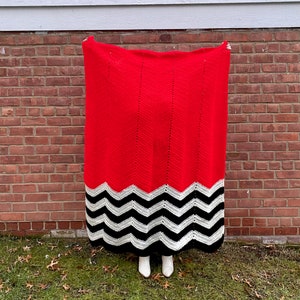 May include: A red crocheted blanket with a black and white chevron pattern at the bottom.
