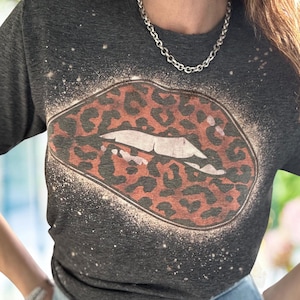 May include: A dark gray t-shirt with a white splatter design and a large orange and black leopard print lip graphic.