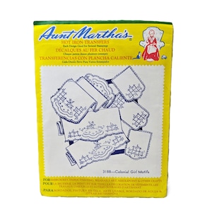 May include: A yellow rectangular package of Aunt Martha's hot iron transfers, model 3188, featuring Colonial Girl motifs. The packaging displays blue line art illustrations of embroidered fabric designs, including figures in dresses and lattice patterns.