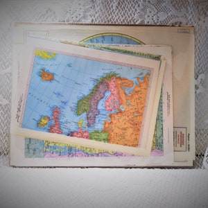 May include: A stack of vintage maps featuring a colorful depiction of Europe and surrounding areas. The maps have a faded appearance with a variety of colors, including blue, green, orange, and pink. The maps are layered on top of each other.