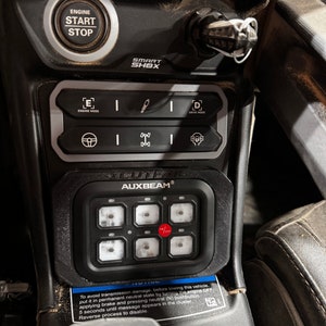 May include: A black dashboard with an engine start/stop button, labeled "ENGINE START STOP". Below are control buttons, including "ENGINE MODE" and "DRIVE MODE". An "AUXBEAM" control panel with six illuminated switches and an on/off button is also visible.
