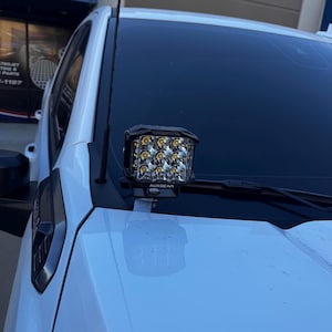 Può includere: Un camion bianco con una barra luminosa a LED AUXBEAM nera montata sul parabrezza. La barra luminosa ha un alloggiamento nero e una lente trasparente con più LED.