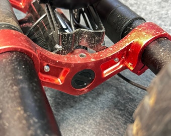 Op de afbeelding: Close-up van een rood metalen fietsframe met een zwart logo. Het frame is bevestigd aan twee zwarte stuurpennen met een zwart en zilveren veersysteem.