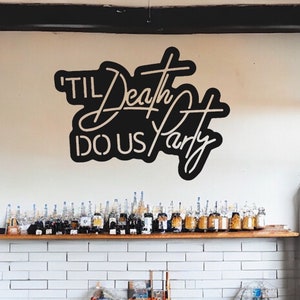 May include: A black and white sign with the text "'TIL Death DO US Party" in a stylized font. The sign is hanging on a white wall above a shelf with rows of glass bottles.