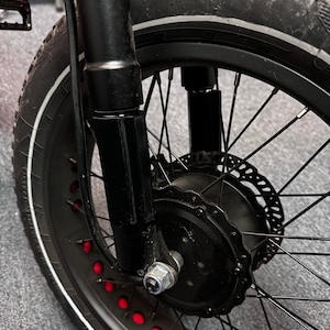 May include: Close-up of a black bicycle wheel with a thick tire and red accents. The wheel has a disc brake and a black suspension fork. The tire has a white stripe along the edge.