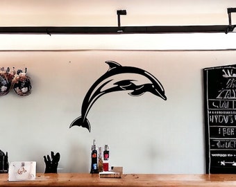 May include: A black silhouette of a dolphin jumping out of the water is on a white wall. There are bottles of liquor on a wooden counter below the dolphin.