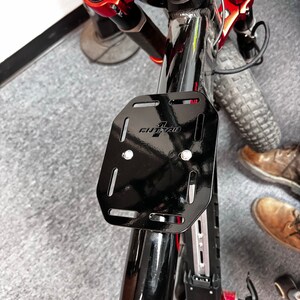 May include: Black metal bike rack with the text "OutRide" on it. The rack is attached to a black bike frame.
