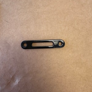 May include: Black metal bracket with two holes and a rectangular cutout.
