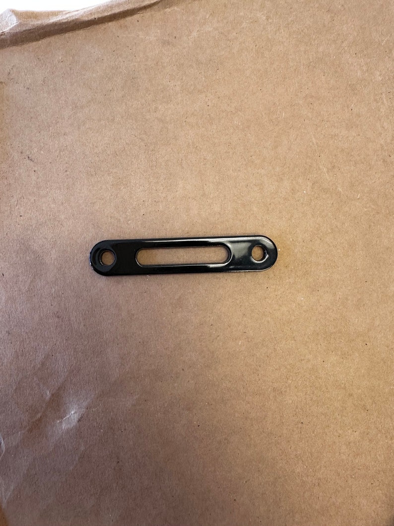 May include: Black metal bracket with two holes and a rectangular cutout.