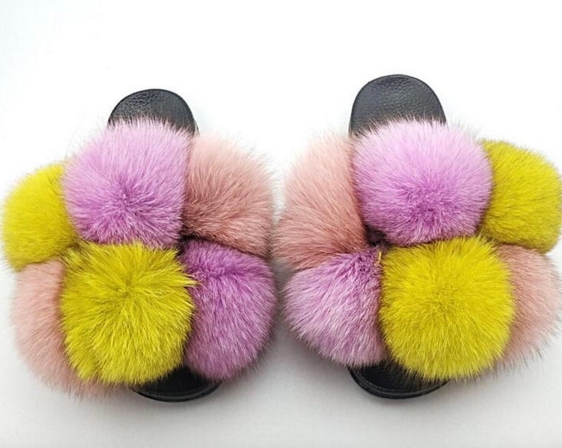 May include: A pair of black fuzzy slides with pink, yellow, and peach colored fur pom-poms.