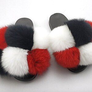 May include: A pair of black fuzzy slides with red, white, and black pom-poms.