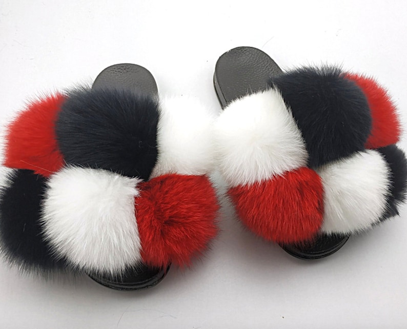 May include: A pair of black fuzzy slides with red, white, and black pom-poms.