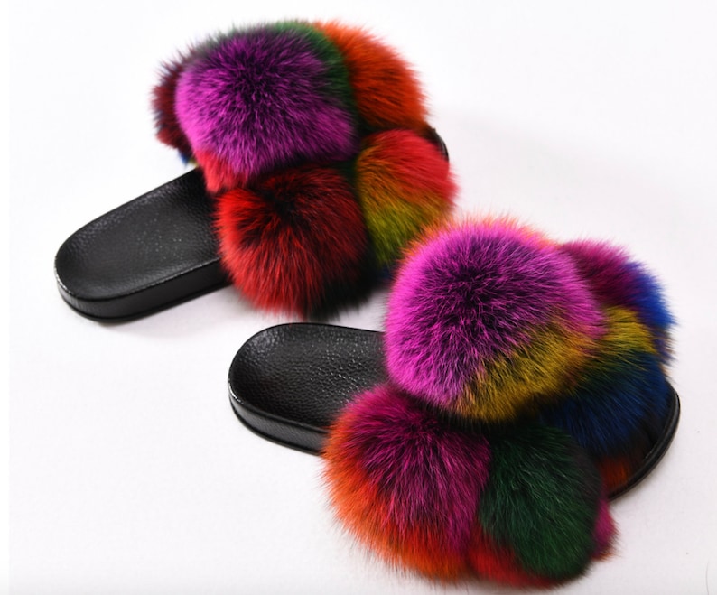 May include: A pair of black fuzzy slides with multi-colored fur pom-poms. The fur is a mix of pink, red, orange, yellow, green, blue, and purple.