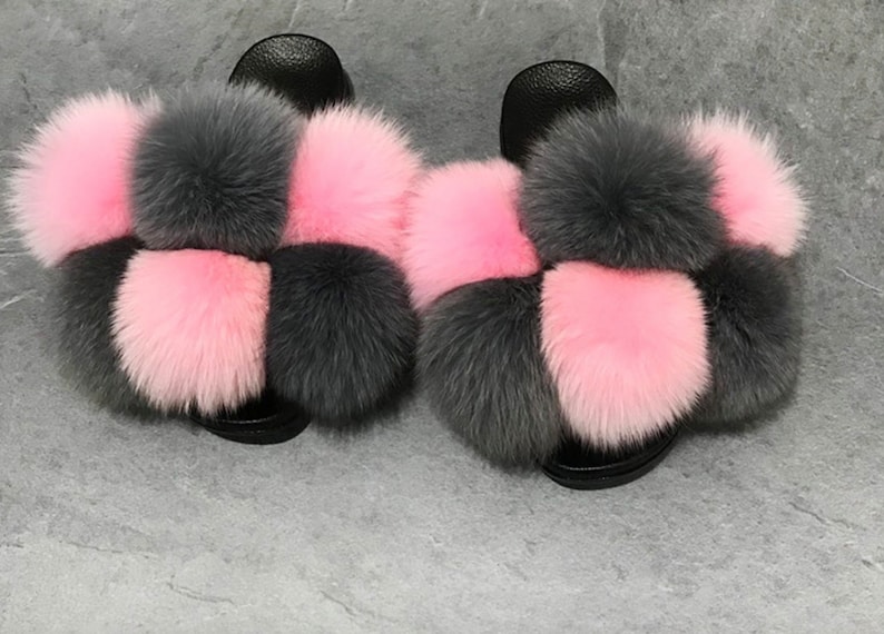 May include: A pair of fluffy slides with a checkerboard pattern of pink and gray fur pom-poms.