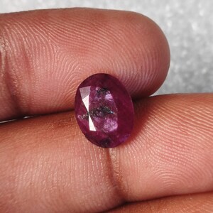 May include: A deep red oval-shaped gemstone with a faceted cut.