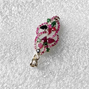 Puede incluir: Un colgante de plata con un diseño de hoja con piedras preciosas rosas, rojas y verdes.