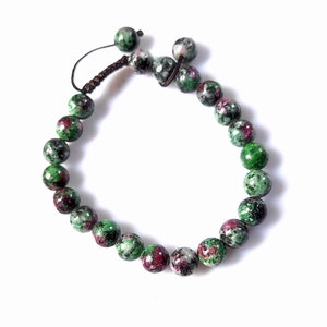 Könnte beinhalten: Ein grünes und pinkfarbenes Edelstein-Armband mit einem geknoteten Kordelverschluss. Das Armband besteht aus runden Perlen mit einem gesprenkelten Muster.