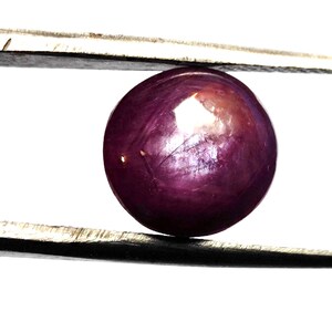 May include: A round, purple star ruby gemstone with a star-like pattern in the centre.