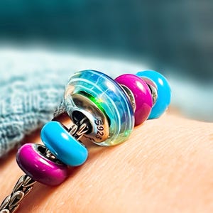 Peut inclure: Un bracelet à breloques en argent avec quatre perles. Les perles sont une perle de verre transparente irisée avec des rayures argentées, une perle rose, une perle bleue et une perle violette.