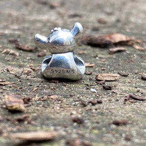May include: Silver charm featuring a cartoon character with large ears and a wide smile. The charm is marked with the text "S925 MS".