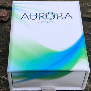 May include: White box with a blue and green abstract design. The box has the text "AURORA - EST. 2017 -" printed on the front.