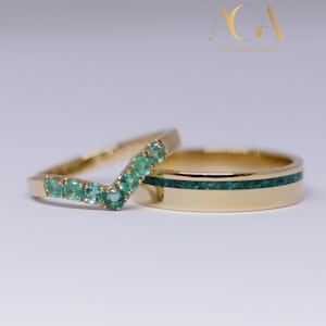 May include: Two gold rings. One ring has a V-shape with small green gemstones. The other ring is gold with a green inlay. The rings are set against a white background. The text "AGA AllanGemsArt" is in the background.