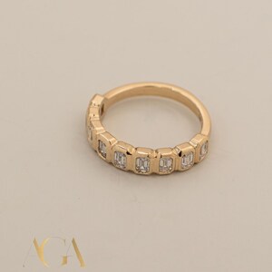 May include: A gold band ring featuring a series of rectangular-cut diamonds. The ring has a polished finish and is set against a neutral background. The ring is a piece of jewelry.
