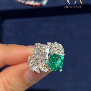 Puede incluir: Un lujoso anillo con un gran diamante de talla cuadrada y una esmeralda vibrante, acentuado con diamantes más pequeños en un diseño de hojas. El anillo está engastado en una banda de oro. El texto "AffanGemsArt" es visible.