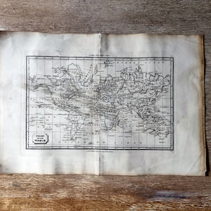 Op de afbeelding: Een antieke wereldkaartprint, met gedetailleerde cartografie van continenten en oceanen. De kaart is gedrukt met zwarte inkt op verouderd papier met kreukels en slijtage. Het papier heeft een lichtbruine tint, met versleten randen.