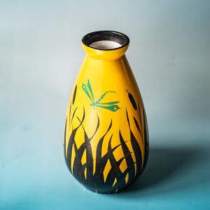Könnte beinhalten: Eine gelbe Keramikvase mit schwarzem Rand und weißem Innenraum. Die Vase hat ein handgemaltes Design aus schwarzen Schilf und einer grünen Libelle. Die Vase ist etwa 25 cm hoch.