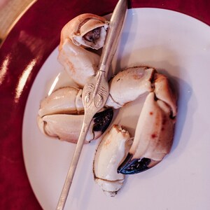 Puede incluir: Un plato blanco con tres pinzas de cangrejo y un cascanueces de cangrejo plateado. Las pinzas de cangrejo están parcialmente abiertas, revelando la carne blanca en el interior.