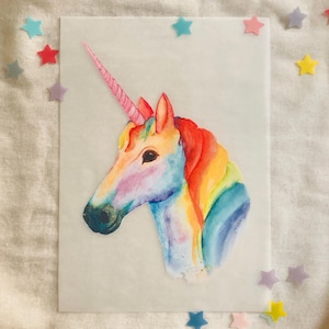 Op de afbeelding: Een aquarel schilderij van een regenboog unicorn met een roze hoorn. Het hoofd en de nek van de unicorn zijn naar de linkerkant van de afbeelding gericht. De achtergrond is wit.