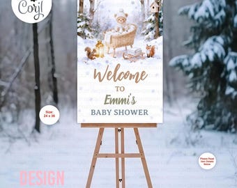 Może przedstawiać: Witamy znak na baby shower na sztaludze. Znak przedstawia zimową scenę leśną z misiem w kołysce, wiewiórkami i napisem "Welcome to Emmi's Baby Shower". Znak ma wymiary 61 x 91 cm.