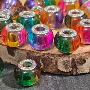 May include: A collection of colorful glass beads with silver accents. The beads are iridescent and have a variety of colors, including red, orange, yellow, green, blue, and purple.