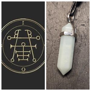 May include: A silver pendant with a white, opaque, crystal-shaped stone. The pendant is attached to a black cord.