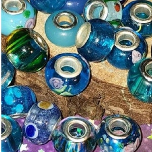 May include: A collection of blue and green glass beads with silver accents. The beads are arranged on a wooden surface and have various patterns and designs.